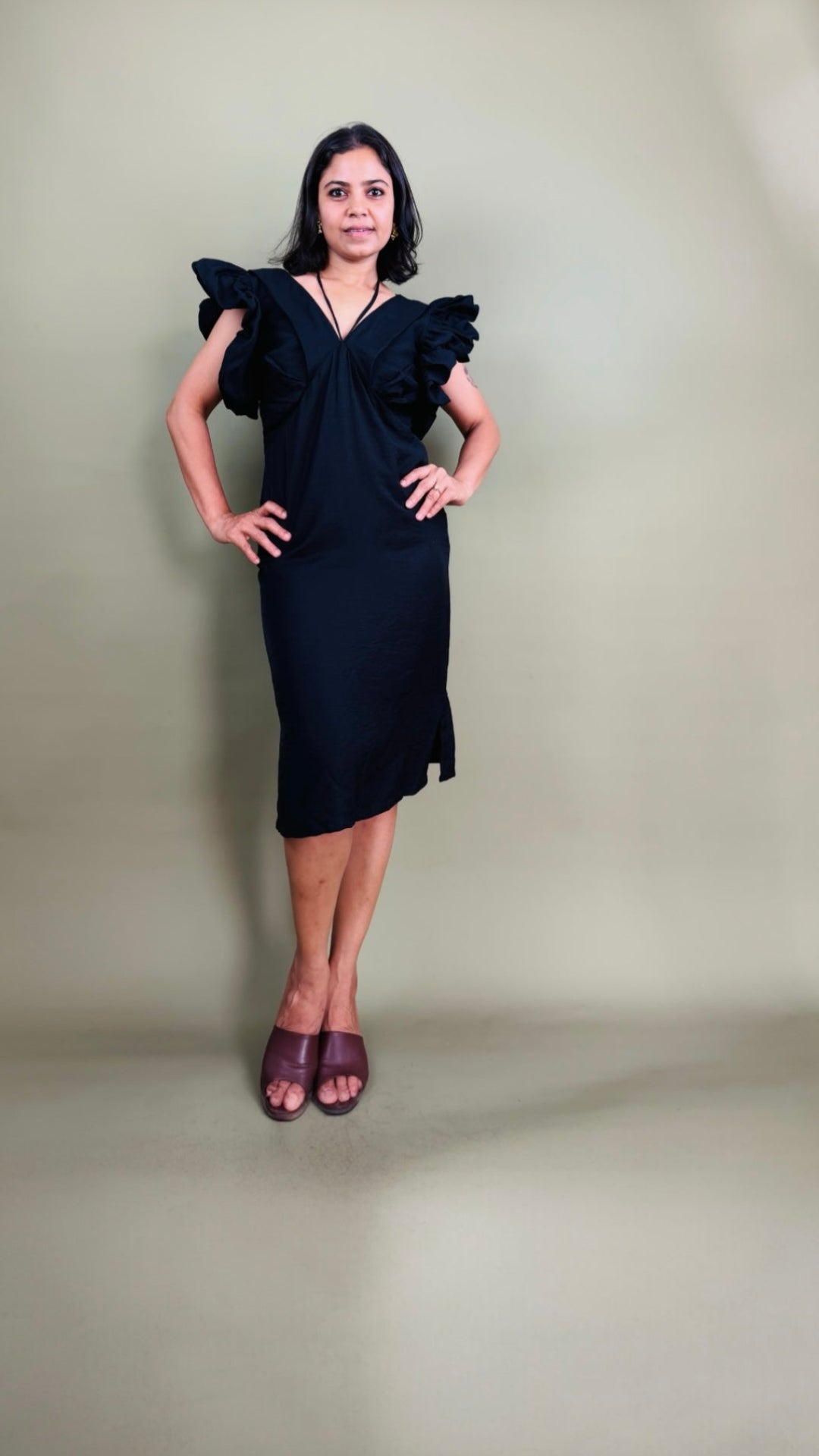 Woman wearing a black dress with ruffled shoulders against a plain background