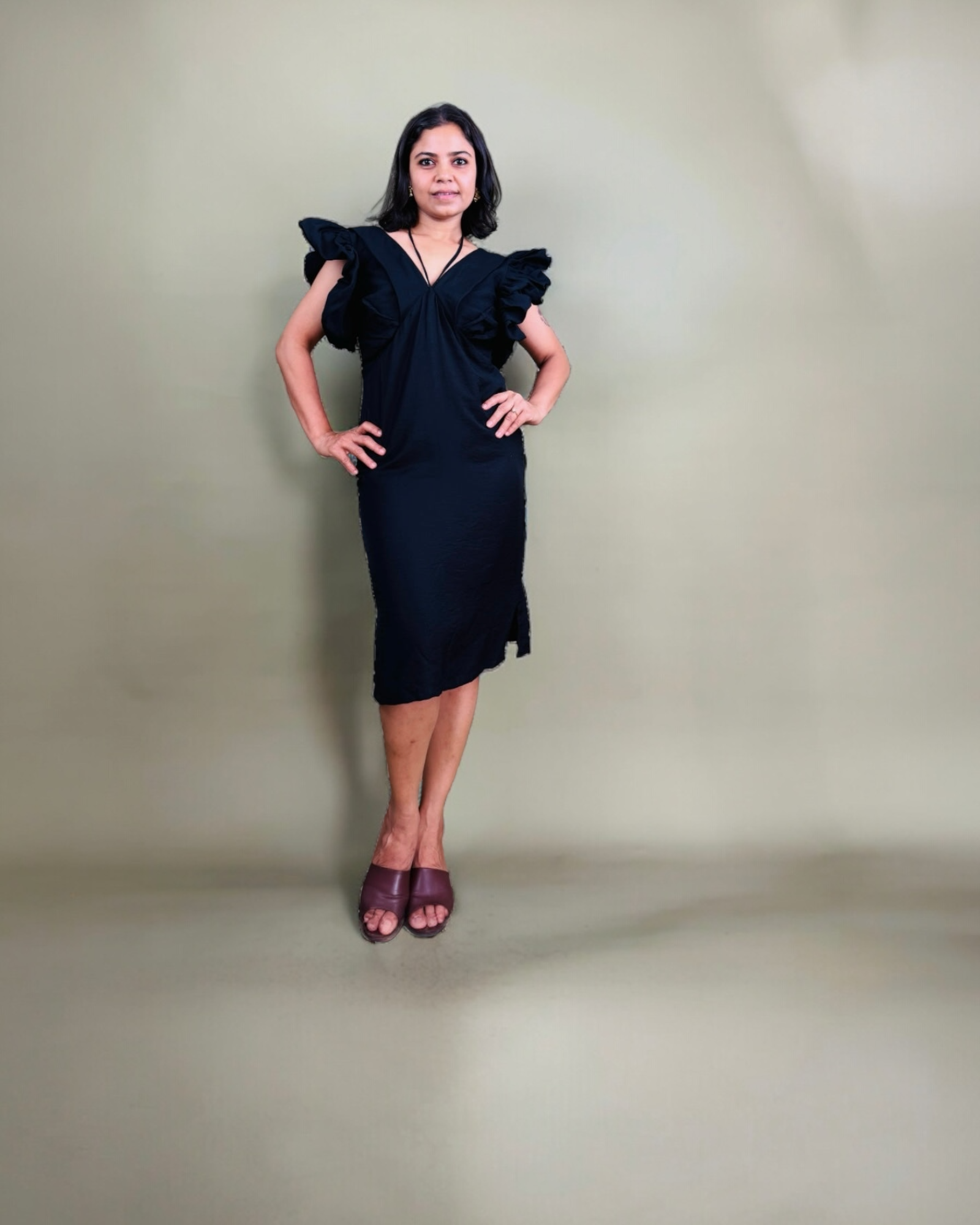 Woman wearing a black dress with ruffled shoulders against a plain background