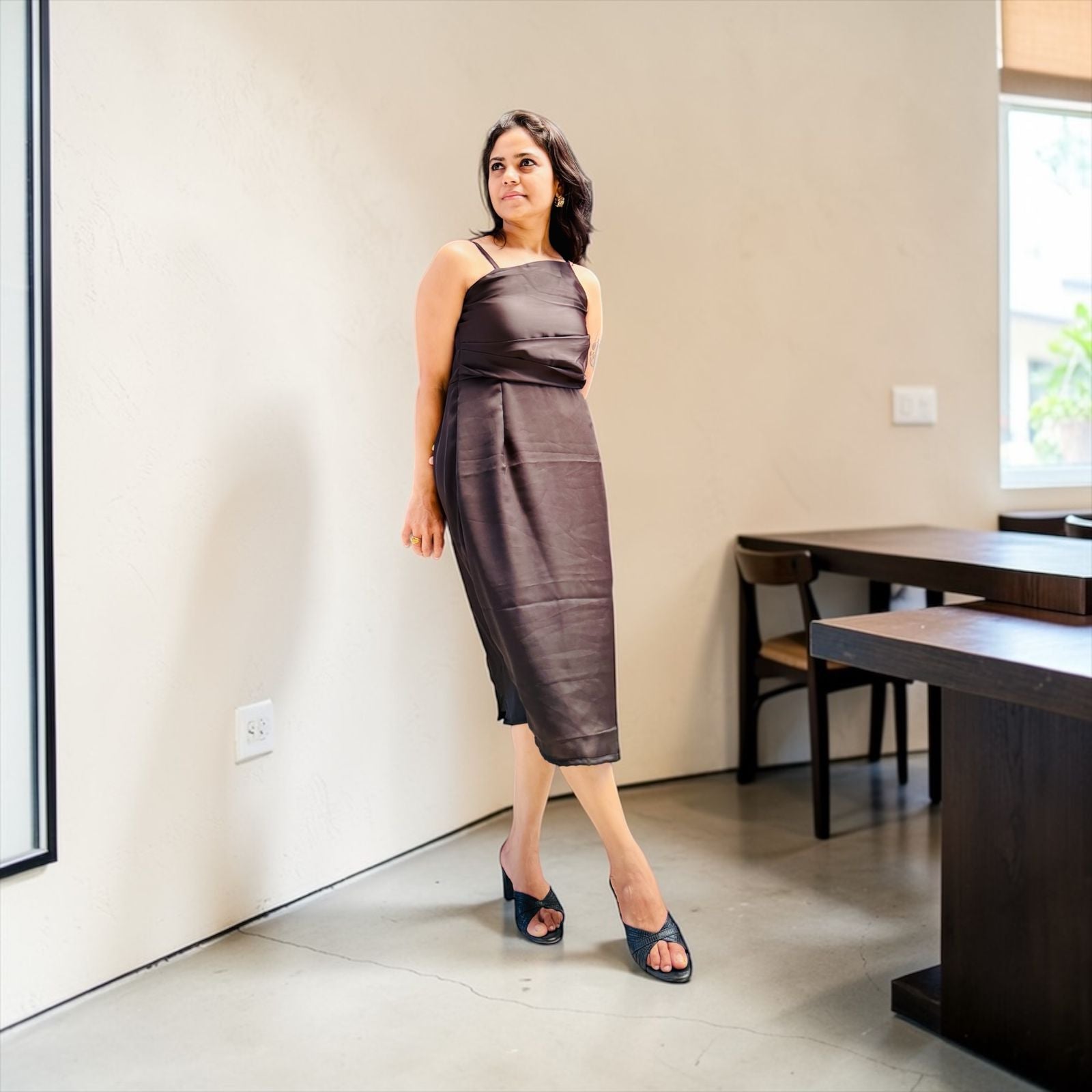 Woman in a brown dress standing in a modern room with neutral decor.